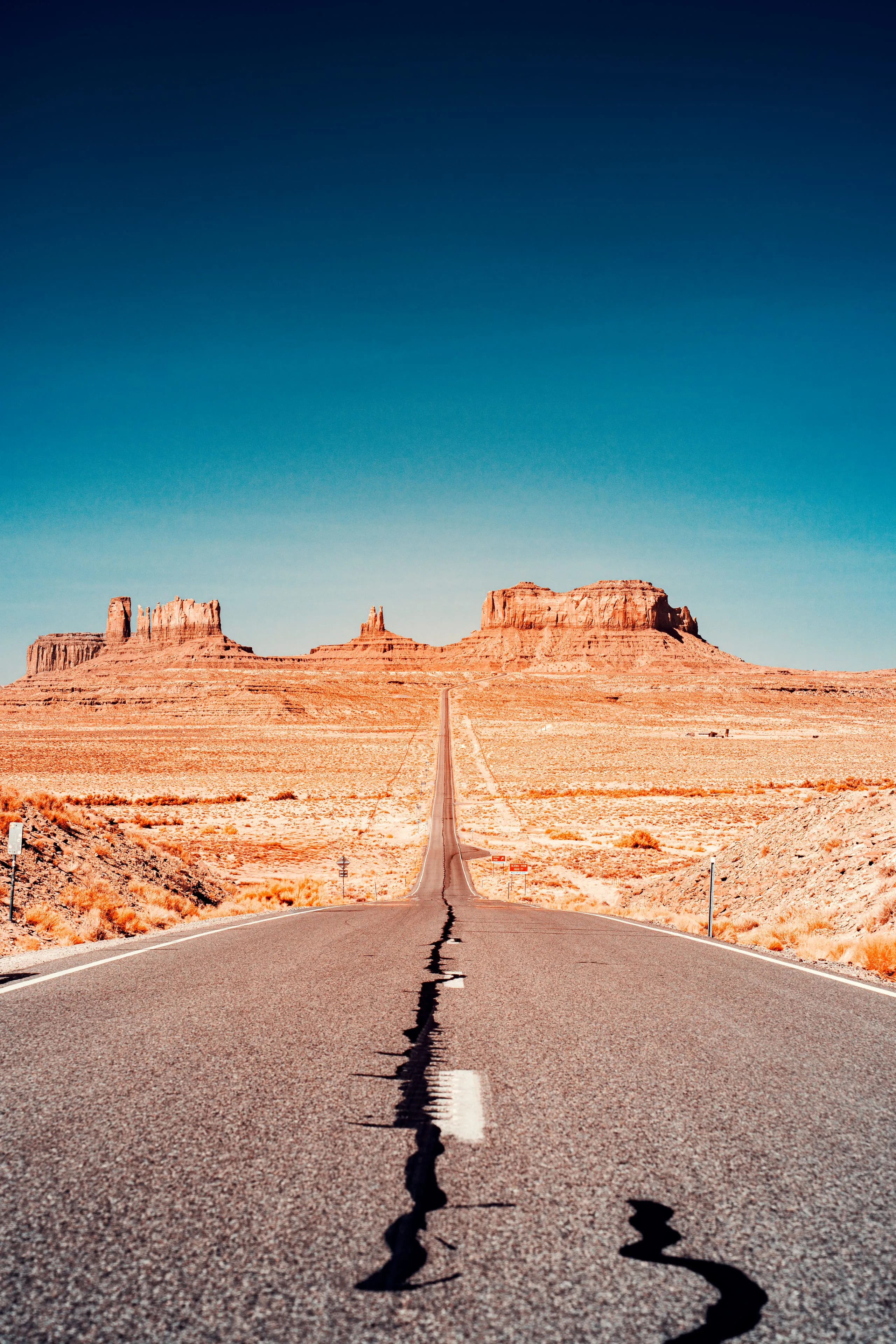 A straight highway runs across golden desert toward the distant buttes of Monument Valley under a deep darkening sky.