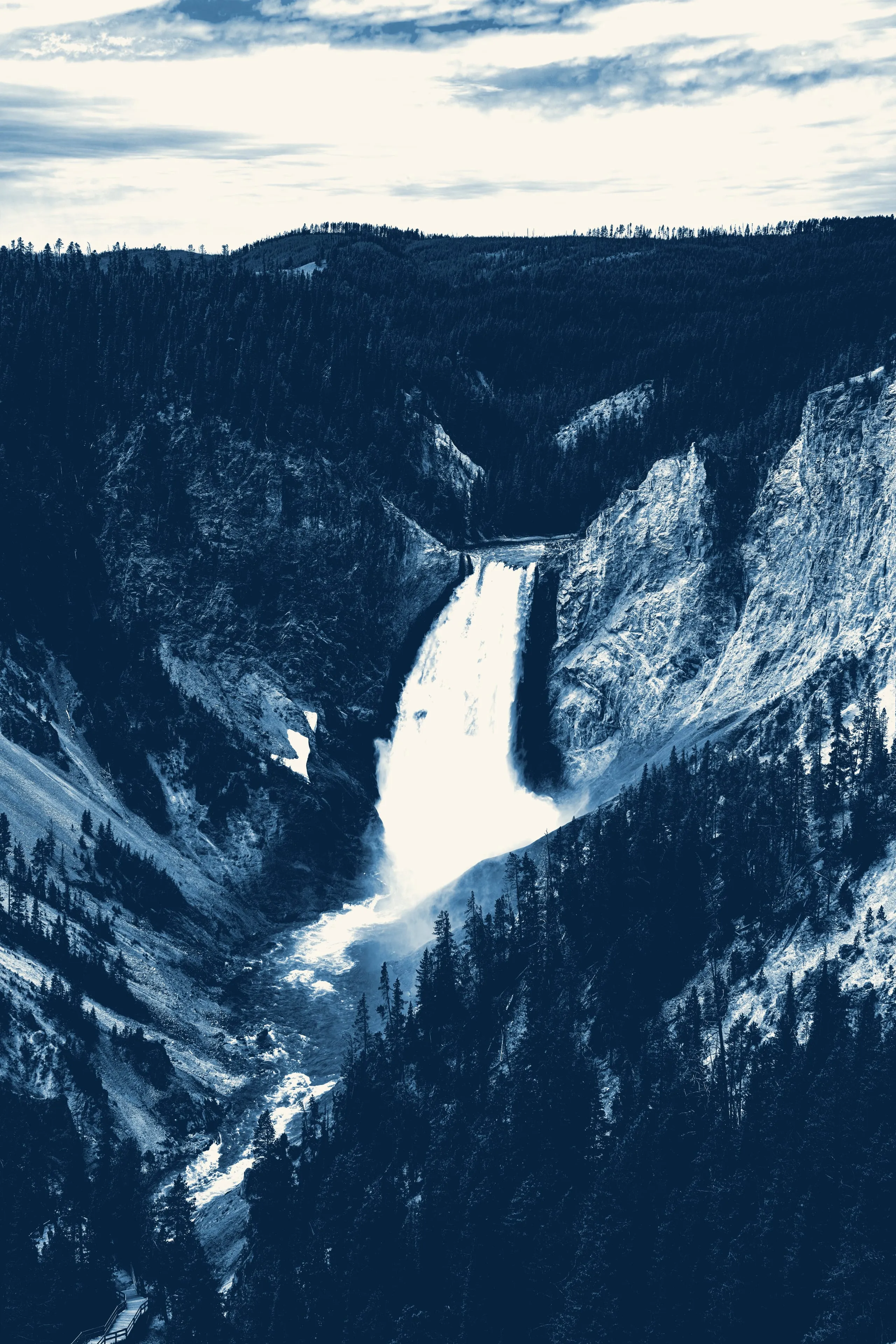 Seen from a canyon rim, a white waterfall plunges into a deep gorge of dark blue rock and conifers, rendered as a cyanotype.