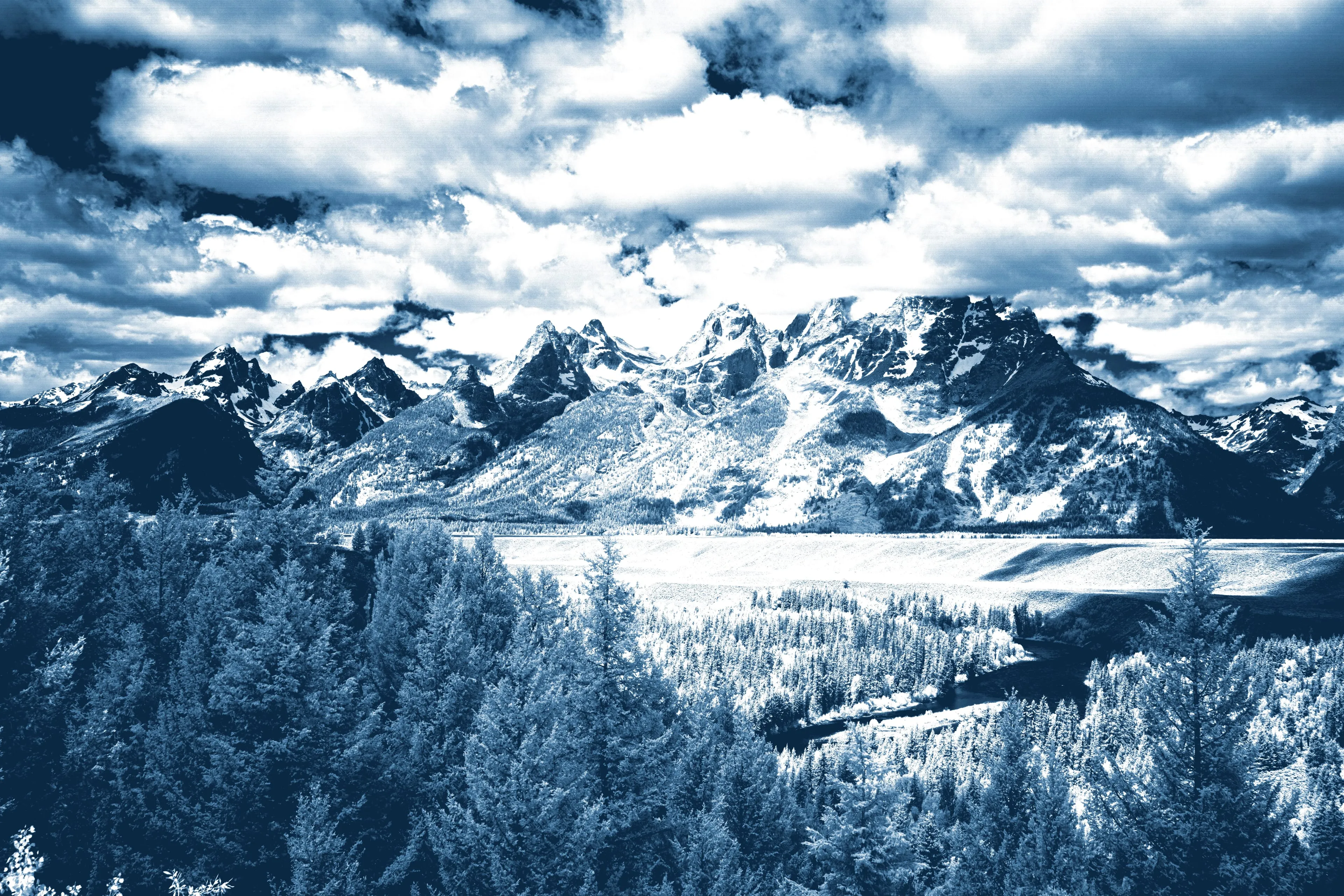 The Teton Range stands over the forested Snake River valley beneath massed cloud; the high peaks and clouds paper-white, the wooded foreground and the winding river deep Prussian blue, rendered as a cyanotype.